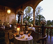 Tische mit Kerzenlicht auf säulengesäumter Veranda eines Restaurants mit Blick auf mediterrane Gartenanlage