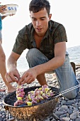 Junger Mann legt Schaschliks auf Grill am Strand