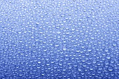 Drops of water on sheet of glass with blue background