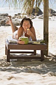 Frau liegt am Strand mit Kokosdrink und isst Ananas