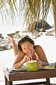 Frau liegt am Strand und trinkt Kokosmilch
