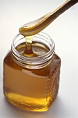 Honig im Glas und auf Holzlöffel