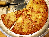Käsepizza mit Pizzaschneider auf Pizzablech