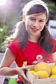 A girl holding a crate of citrus fruits