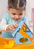 A little girl making a paper bird house