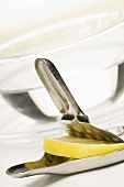 A lemon press with a slice of lemon and a tea cup in the background