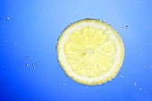 A slice of lemon in blue water with air bubbles