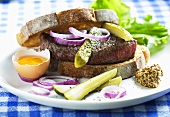 A beef sandwich with gherkins, egg, onion and mustard