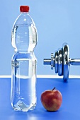 A bottle of mineral water, an apple and a dumbbell