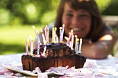 A birthday cake with burning candles and a young woman in the background