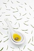 A spoon of olive oil and an olive and scattered rosemary leaves