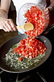 Frau schüttet Tomatenwürfel in Pfanne am Herd