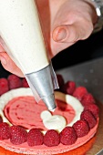 A raspberry cake being decorated with vanilla cream