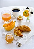 Breakfast with melon, croissant, egg, jam, coffee and orange juice