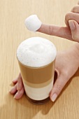 Milk foam covered finger from a glass of Latte Macchiato