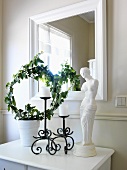 Venus-Statue, Kerzenhalter und Pflanzendekoration auf weißem Garderobentisch vor Spiegel