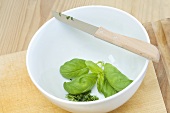 Partially chopped basil in a bowl with a knife