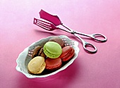 Different types of macaroons in a porcelain dish with a pair of tongs next to it