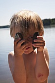 Kleiner Junge am See hält zwei Muscheln in den Händen