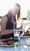 Weissweinglas, im Hintergrund Frau beim Essen