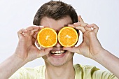 A young man holding orange slices in front of his eyes