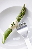 A green asparagus spear with sauce Hollandaise and a fork