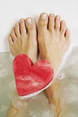 Füße und ein herzförmiger Schwamm in einem Bad