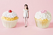 A woman standing between two cupcakes