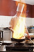 A chef cooking in a commercial kitchen, partially hidden behind a flame