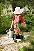 A little girl dressed as a gardener with a watering can
