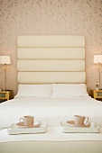 Stilvolles Schlafzimmer mit Doppelbett, grossem Kopfteil & zwei Tabletts mit Kaffeetassen auf dem Bettende