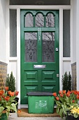 Hauseingang mit Frühlingsblumen in Töpfen & Recycling-Box vor grüner Haustür