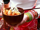 African woman holding bowl of scampi & spinach risotto