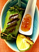 Rice parcels in banana leaf; chili sauce; lime