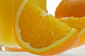 Wedge of orange in front of glass of orange juice (close-up)