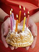 Hands holding small fruit cake with burning candles