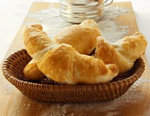 Freshly baked croissants in bread basket on chopping board