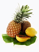 Pineapple, papayas and coconut on palm leaf