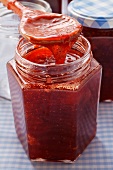 Strawberry jam in jar and on kitchen spoon