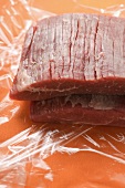 Raw flank steaks on clingfilm
