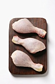 Three raw chicken legs on chopping board