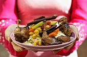 Woman serving roast pigeon with vegetables on noodles (Morocco)