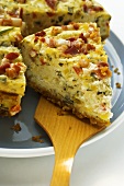 Leek and bacon quiche, a piece cut, with piece on server