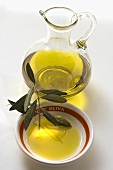 Olive oil with olive branch in bowl in front of carafe