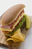Sub sandwich with crisps and gherkin on chopping board