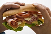 Hands holding ham and cheese sub sandwich