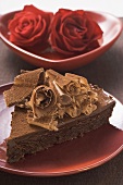 Piece of chocolate cake with chocolate curls, red roses