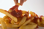 Hand nimmt Pommes frites mit Ketchup