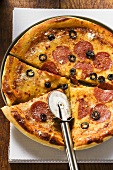 Pizza with salami, cheese and olives with pizza cutter
