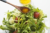 Olive oil in wooden spoon above salad leaves